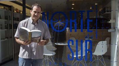 Mikel de Elguezabal con un libro frente a su café-librería Al norte del Sur, situado en la plaza Consistorial de Pamplona (foto Unai Beroiz-Diario de Noticias)